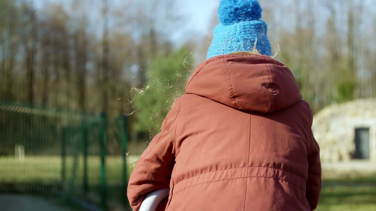 niña linda con sombrero azul jugando en el patio de recreo. hembra encendiendo el carrusel y sonriendo. infancia despreocupada