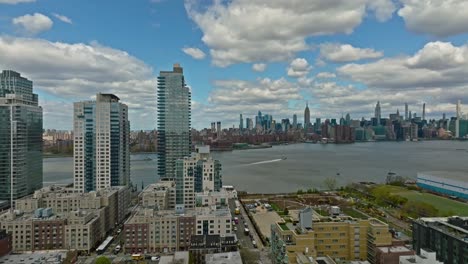 aerial view of luxury mirrored building at waterfront of greenwich brooklyn district with view on new york city skyline behind east river - slow forward flight