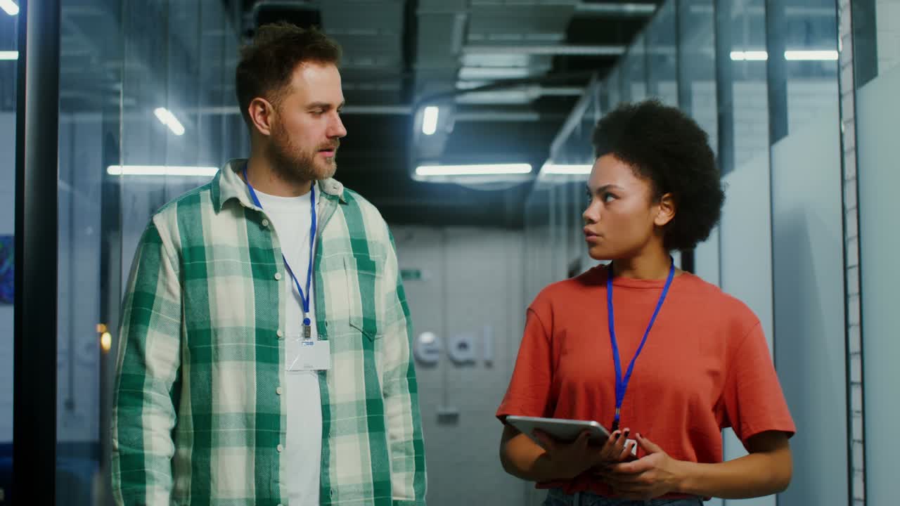 jóvenes colegas usan una tableta y hablan mientras caminan por el centro de la oficina