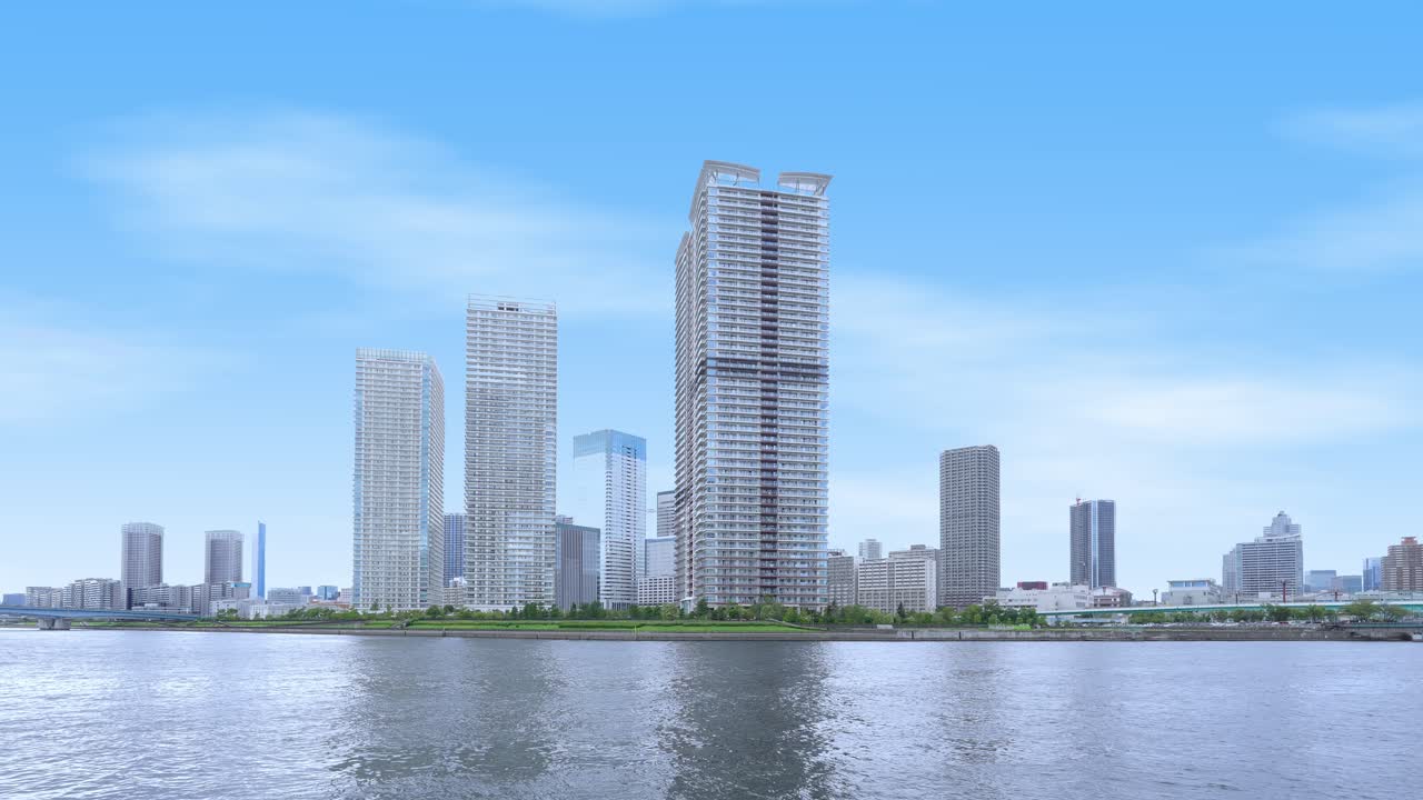 A peaceful wide shot of the Tokyo skyline from a waterfront promenade with modern high-rise buildings and a clear sky
