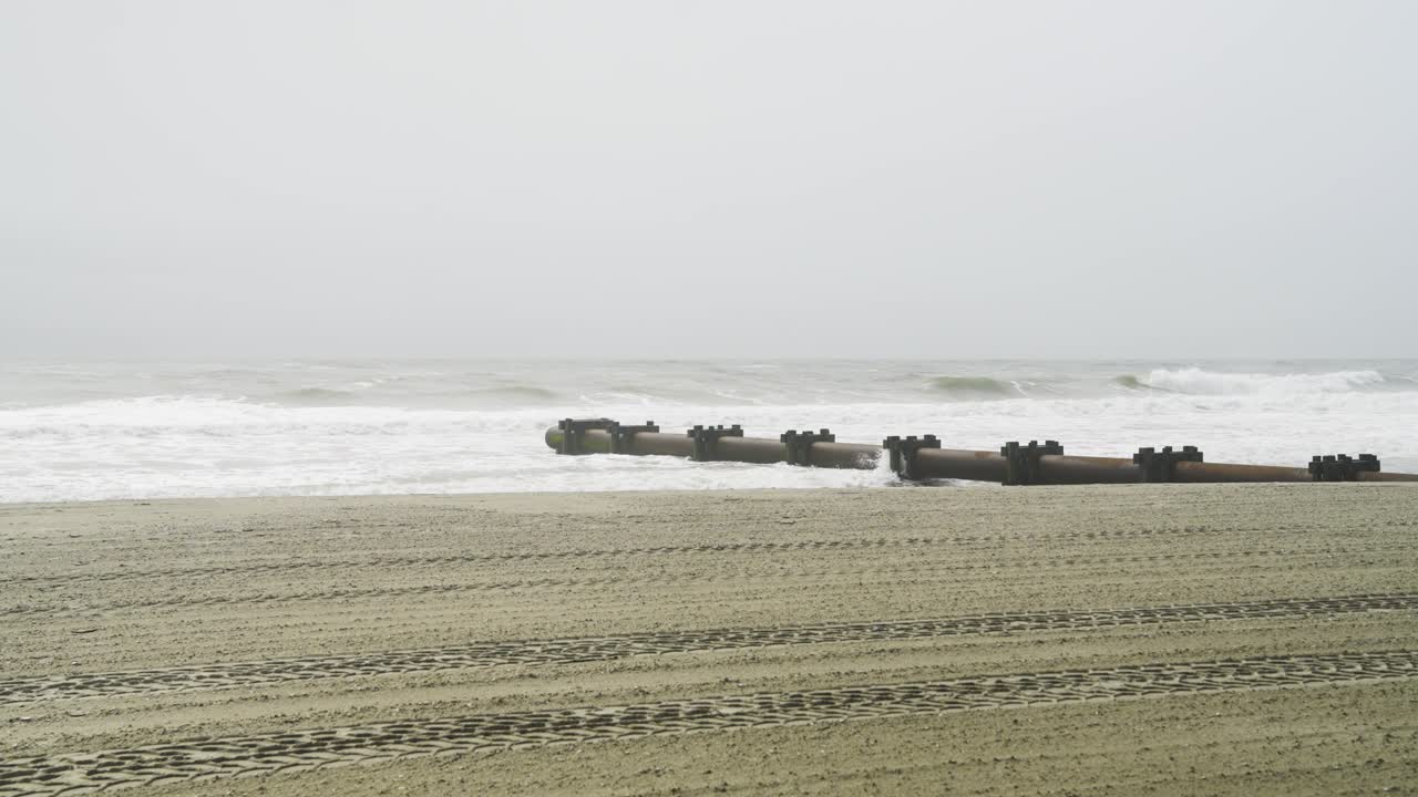 Rough ocean waves hitting pipeline on beach with tire tracks on a gloomy day in OCNJ