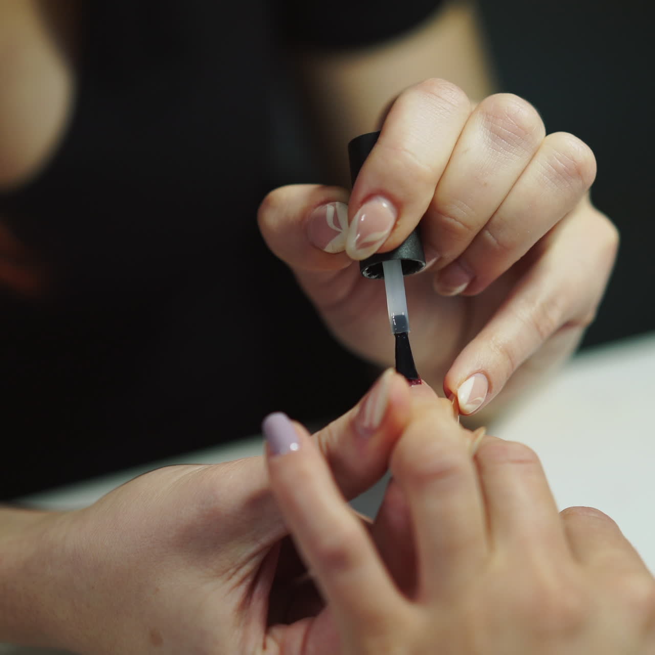 Professional nail artist applies finish layer of clear nail polish on woman's nails with manicure in salon. Master does manicure procedure to a female in the beauty center. Close-up