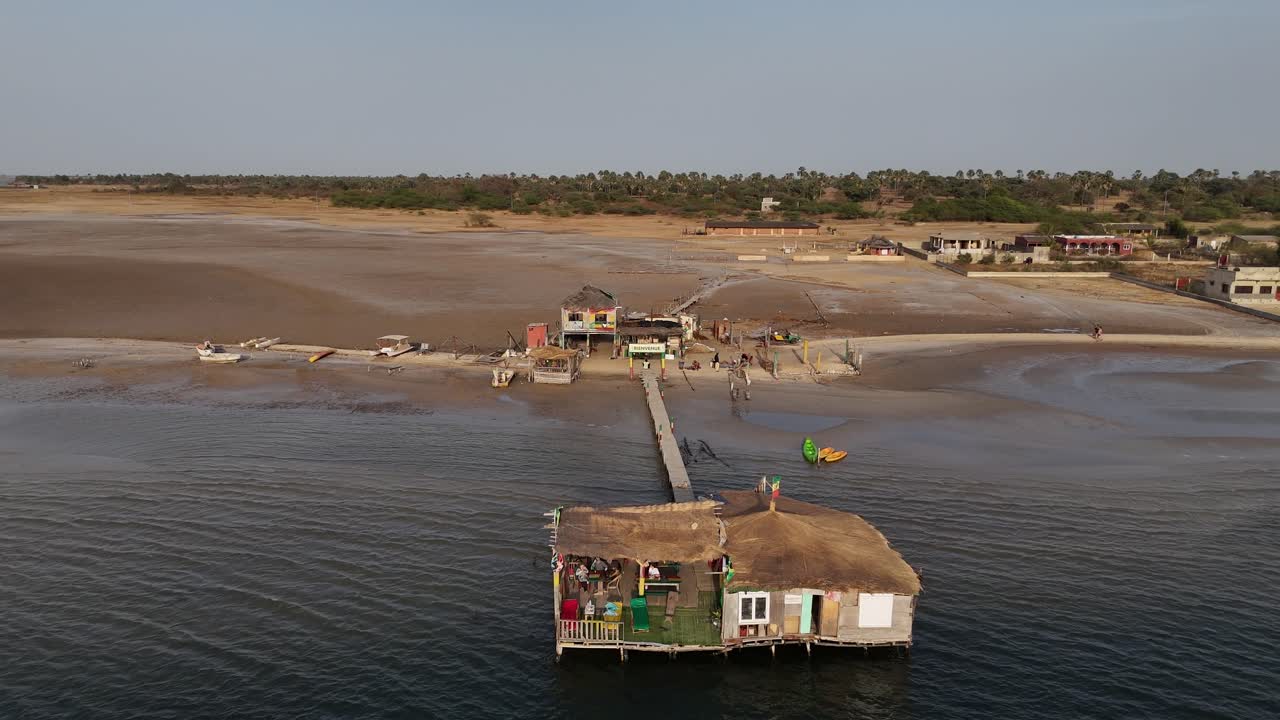 Aerial drone footage of sandy beach and wooden piers in Sine Saloum Delta, Senegal. Scenic coastal landscape with fishing boats and local waterfront activity