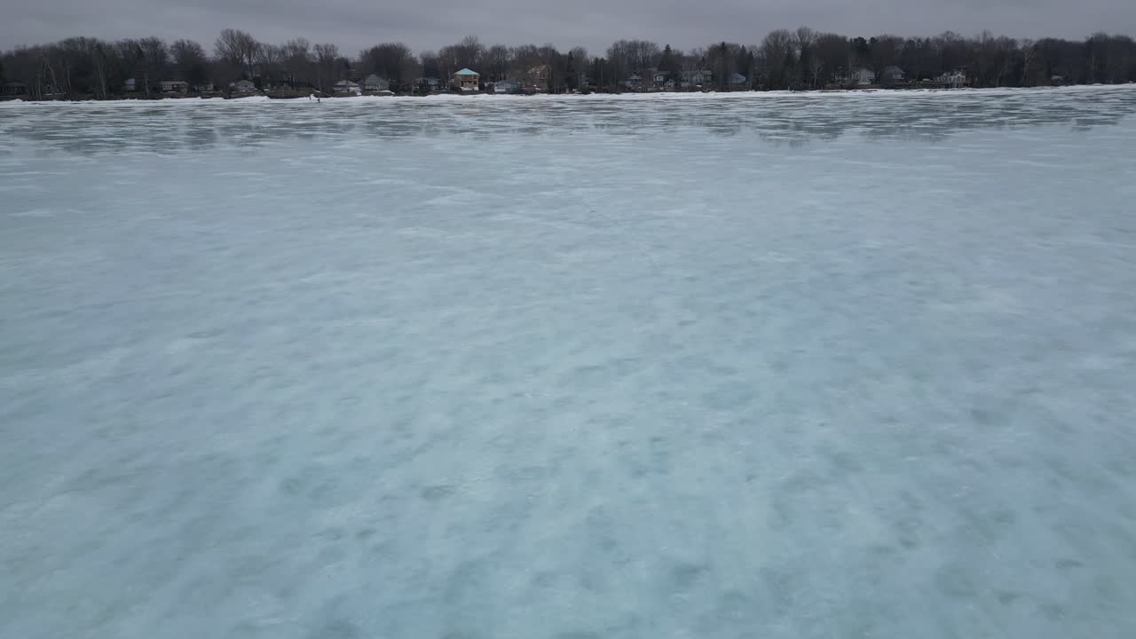 4K drone shot of a frozen lake with large cracks in the ice. . Also visible are the cottages along the shore of Lake Simcoe in Ontario Canada.
