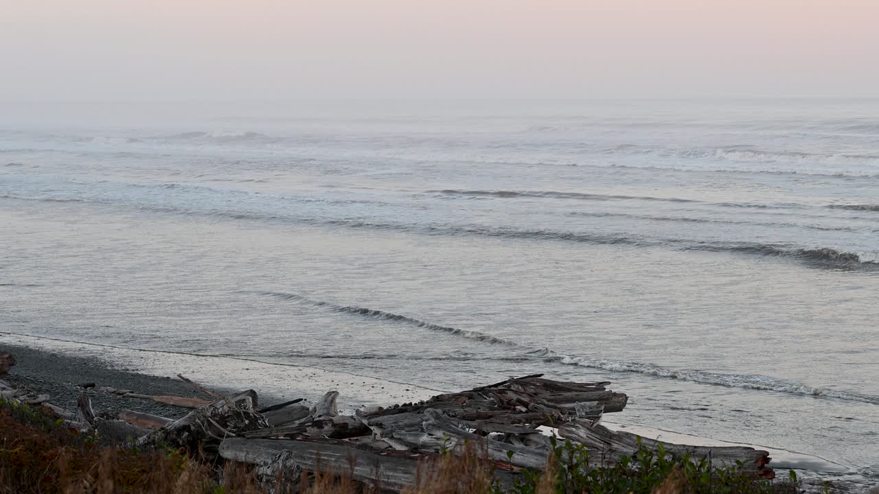 Rocky sea stacks rise above the surf as waves crash on a misty shoreline at sunset