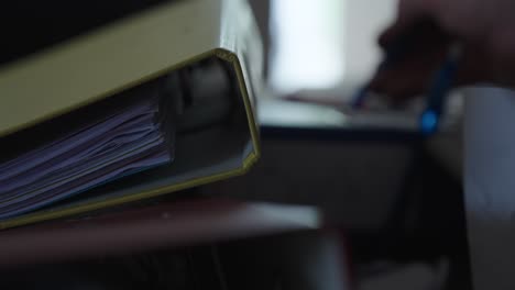 a yellow binder dominates the foreground while someone writes in the background—capturing a quiet moment of focused work or documentation