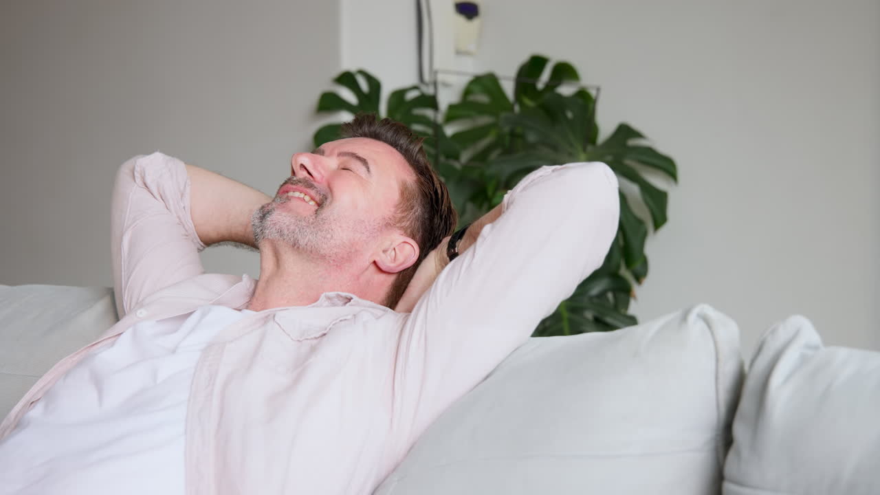 Relaxing at home, senior man smiling with hands behind head on couch