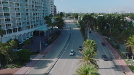 Forwards-tracking-of-vehicles-on-multilane-trunk-road-lined-by-grown-palm-trees.-Modern-city-borough-in-tropic-area.-Miami,-USA