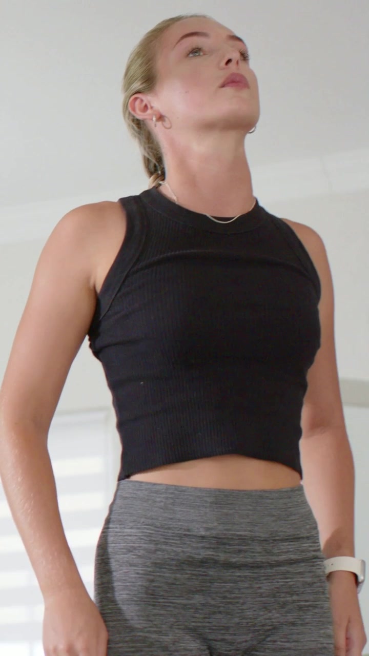 Vertical video: Camera panning woman modeling leggings, lifting chin at home by sofa, copy space