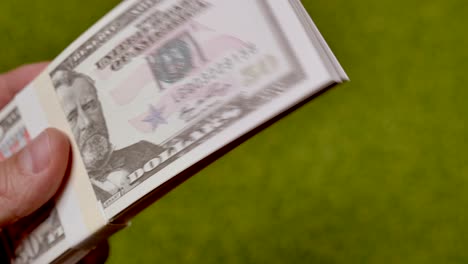 Man-holding-pile-of-fifty-us-dollar-banknotes-outdoors-on-grass-field