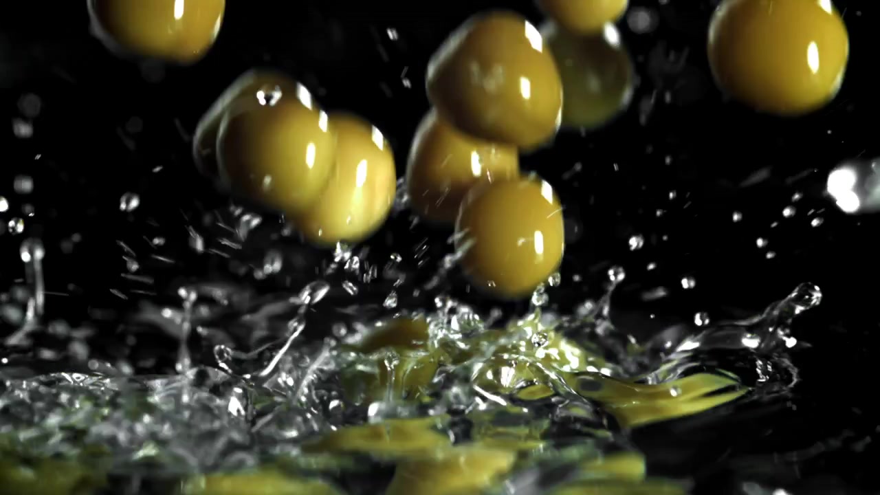 Olive verdi che cadono e schizzano nell'acqua al rallentatore.