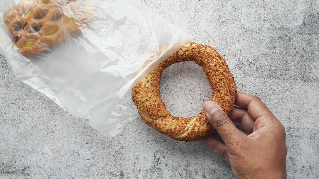 mano sosteniendo un pan simit con otro pan en una bolsa de plástico