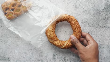 hand holding a simit bread with other bread in plastic bag