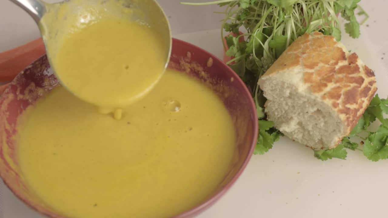 Serving carrot and coriander soup with ladle medium shot