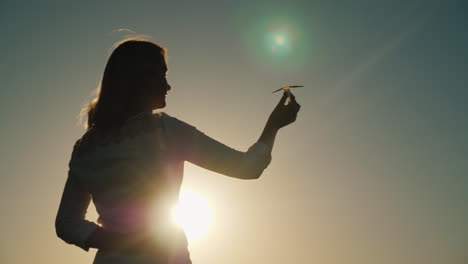 a woman is playing with a paper airplane it stands in the rays of the setting sun dreams about vacat