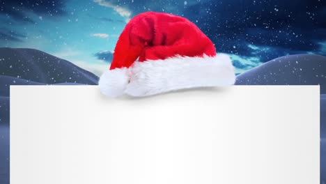 Santa-hat-over-a-blank-placard-against-snow-falling-on-winter-landscape