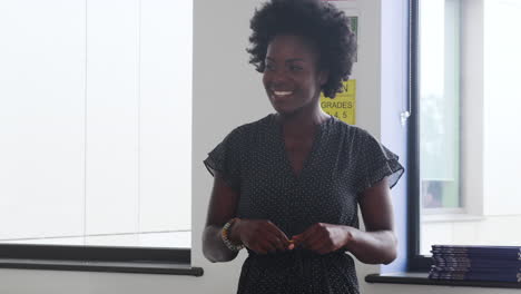 Female-High-School-Tutor-Standing-By-Table-With-Students-Teaching-Lesson