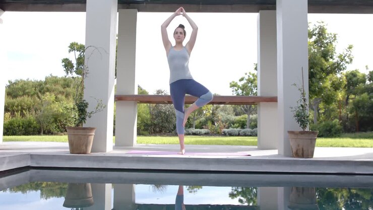Ritratto di donna caucasica concentrata che fa una posa yoga su un tappetino in giardino al rallentatore.