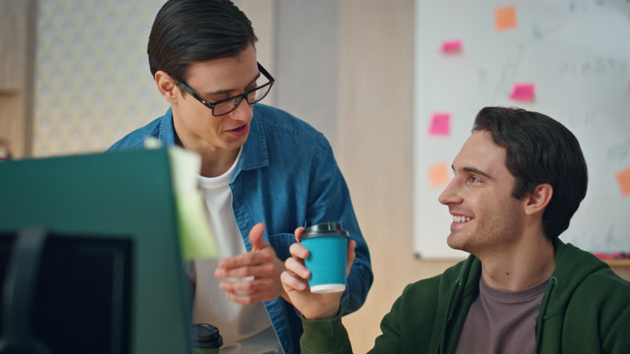안경 남자가 동료 사무실에 커피를 주고 있다. 디자이너들이 토론하고 있다.