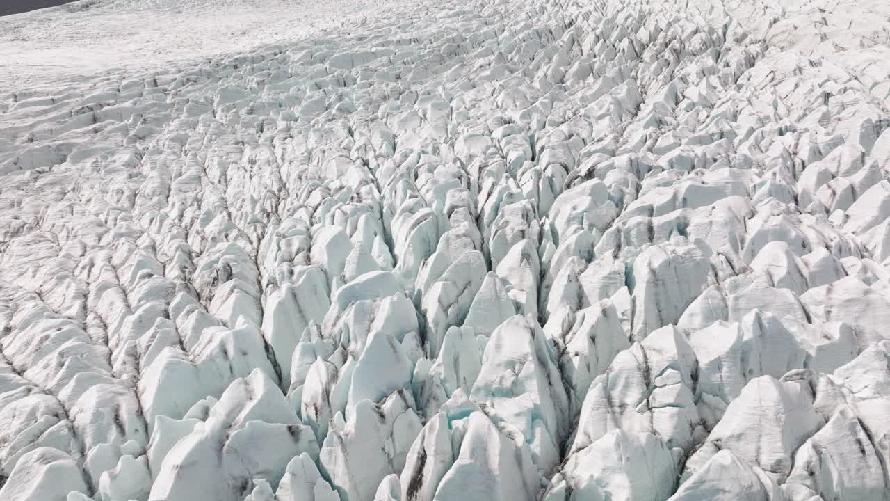 A breathtaking aerial view of Fjallsjökull Glacier, Iceland, showcasing sharp, jagged crevasses and icy formations stretching across the frozen terrain.