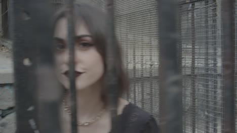 young adult woman with dark makeup defying camera trapped into a cage gray tones