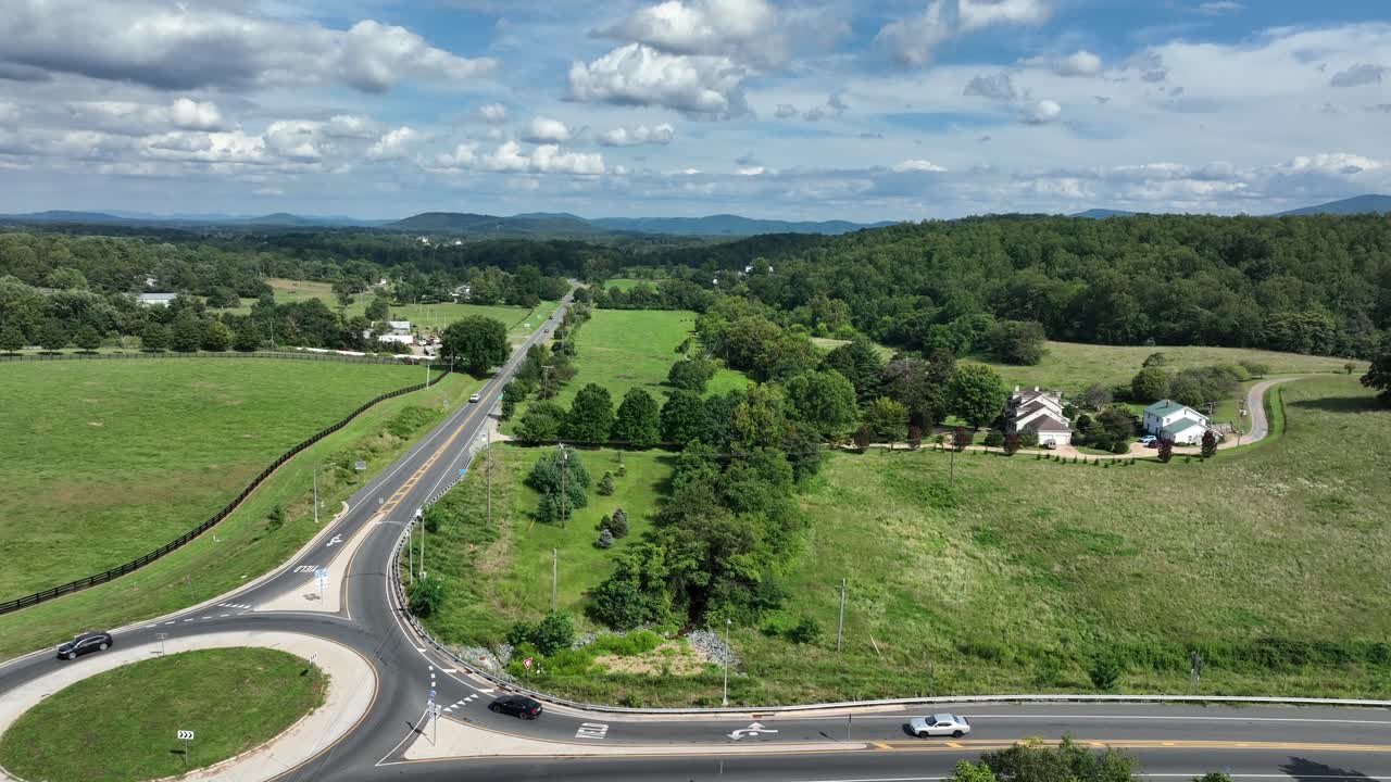 Traffic in roundabout and rural street of American countryside. Descend drone wide shot. Sunny summer day in suburbia of town in Virginia, USA. Farmstead and property in quiet suburbia