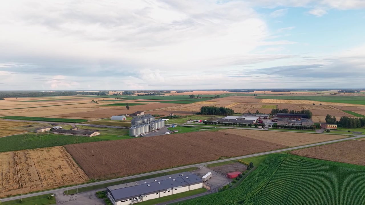 Ampie riprese aeree catturano vaste terre agricole rurali, silos industriali, campi ed edifici agricoli sotto un cielo luminoso, offrendo un dinamico paesaggio agricolo con luce naturale nitida