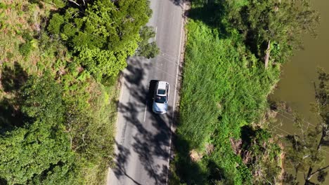 drone captures a car driving through lush greenery and trees along a winding road in new south wales, australia