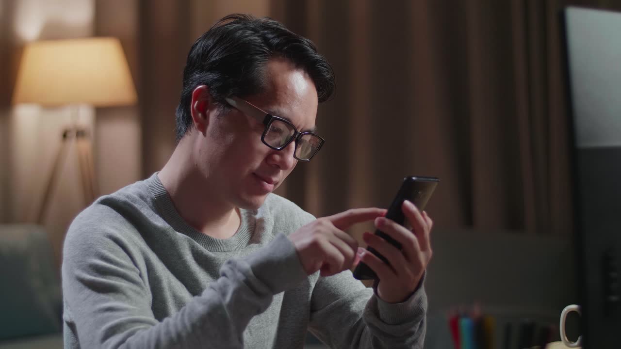 아시아 남성 신발 디자이너가 집에서 데스크 컴퓨터에서 작업하는 동안 스마트폰을 찾고 있습니다.