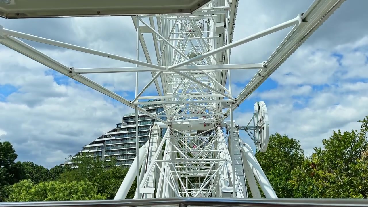 Ferris wheel structure under a cloudy sky with greenery in the background