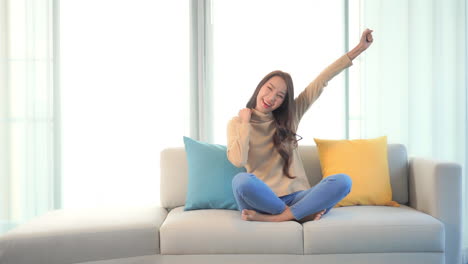 a young woman sitting on a couch expresses her enthusiasm by thrusting her arms in the air with joy