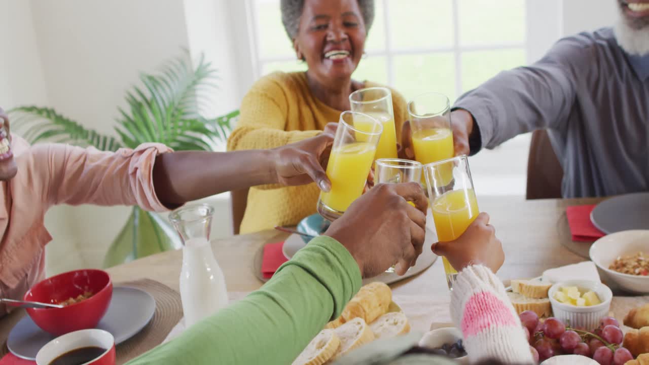 video de padres afroamericanos felices, hija y abuelos haciendo un brindis en la mesa de la cena