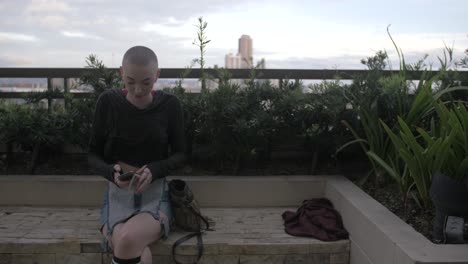 a pretty woman with short hair enjoying a rooftop garden takes her phone from her purse and talks