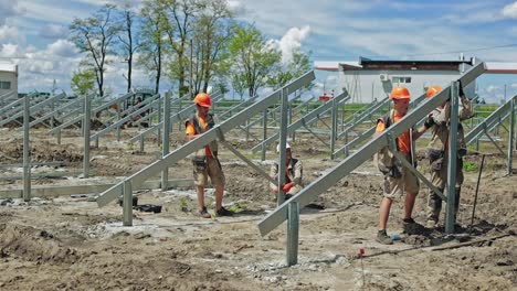 engineers putting metal construction on the ground. group of workers in hard hats build metal basis for solar panels on the field in summer day.
