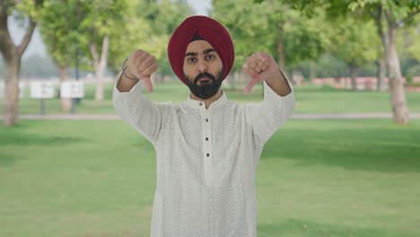 disappointed sikh indian man showing thumbs down in park