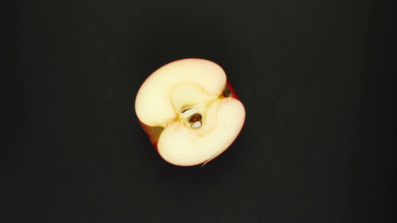 Roterende æble på sort baggrund. Friske juicer, frugter, vitaminer og sommerkoncept. Topudsigt af et halvt saftigt æble