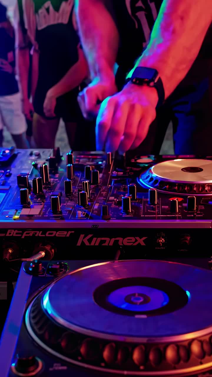 Close-up video shot of a DJ's hands mixing music on a console at a beach party, capturing vibrant
