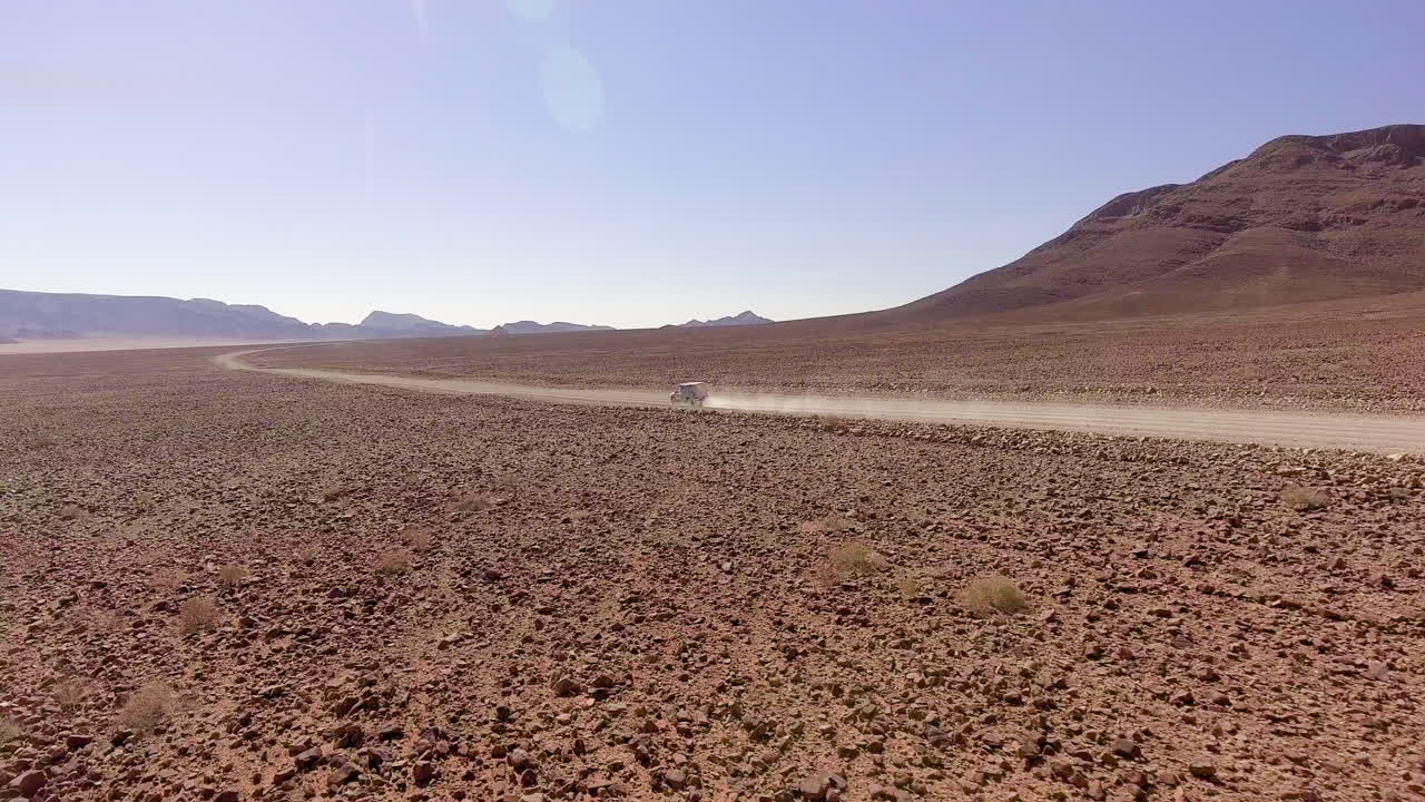 Car raising dust trail driving through Namibia rocky desert, Aerial Pan