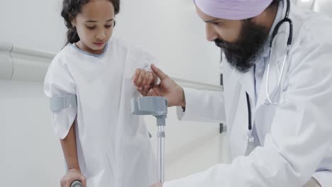 happy biracial doctor talking to sick girl patient with crutches in slow motion