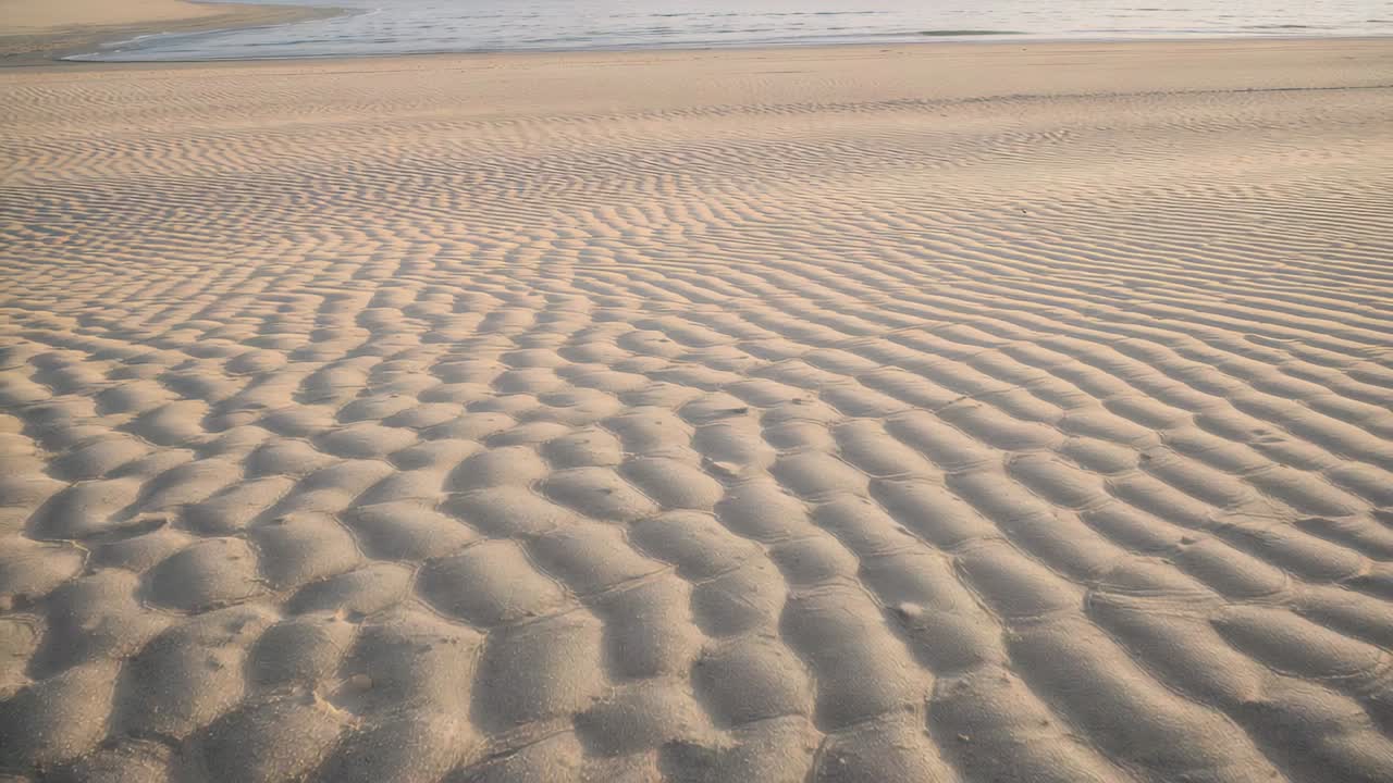 Panning camera revealing rippled beach sand at low tide, highlighting tidal channel and shells