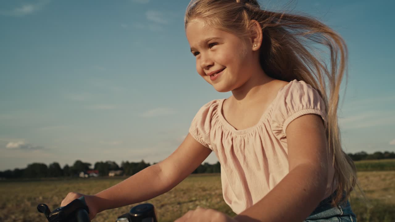 Aufnahme von unten: Kaukasisches Mädchen im Grundschulalter fährt bei Sonnenuntergang Fahrrad.