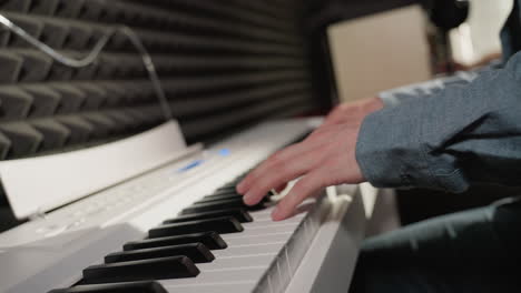 side view of a musician's hand wearing a blue long sleeve shirt playing a white piano, with a black acoustic wall in the background. the focus is on the piano keys and the hand