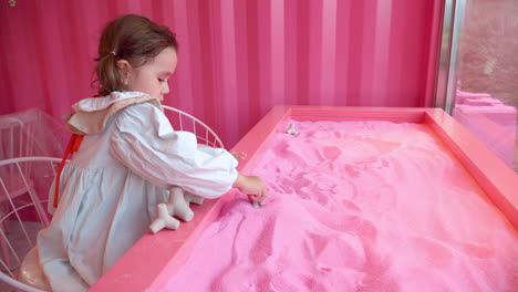 little girl toddler playing with pink sand sitting bytable and submerging toy tetrapods into purple sand at herb island farm in pocheon