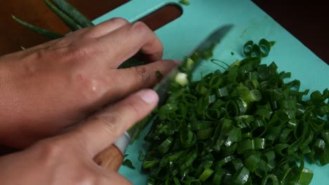 top view of women's hands cut green onions with a knife on a board