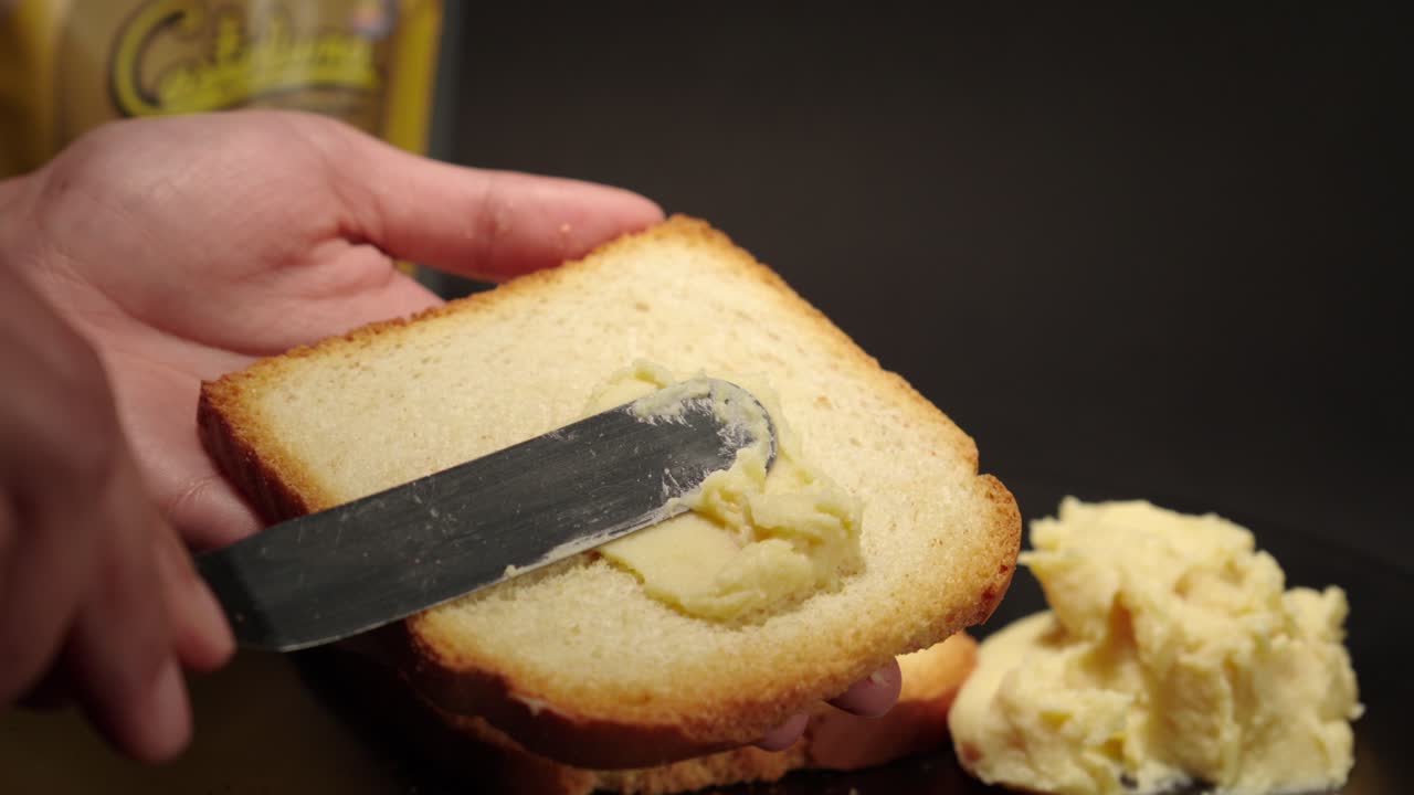 Butter cheese smooth soft creme peanut jelly putting on top of a toast of bread slice slow motion with black background female hands