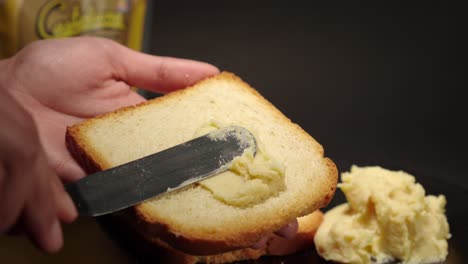 butter cheese smooth soft creme peanut jelly putting on top of a toast of bread slice slow motion with black background female hands