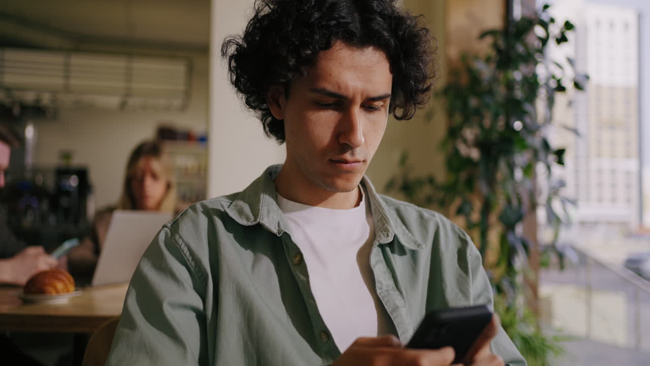 A man sitting at a table in a cafe, looking at his phone.