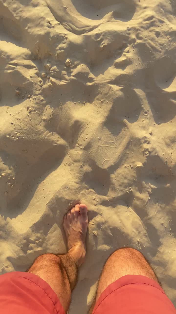 Video in stile UGC POV con ripresa dall'alto di una persona che cammina su una spiaggia sabbiosa verso il mare. Vacanze estive. Uomo con costume da bagno che cammina sulla sabbia per fare una nuotata durante una calda giornata estiva