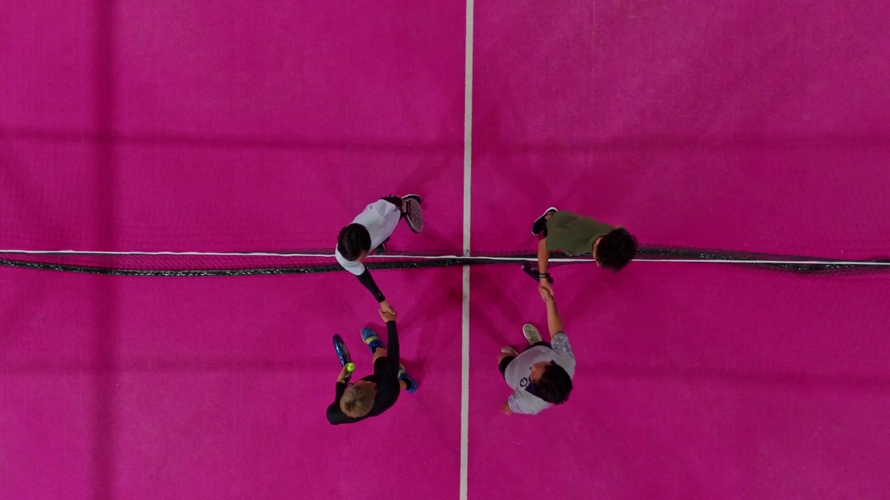 Giocatori di padel tennis che si salutano sopra la rete su un campo rosa.