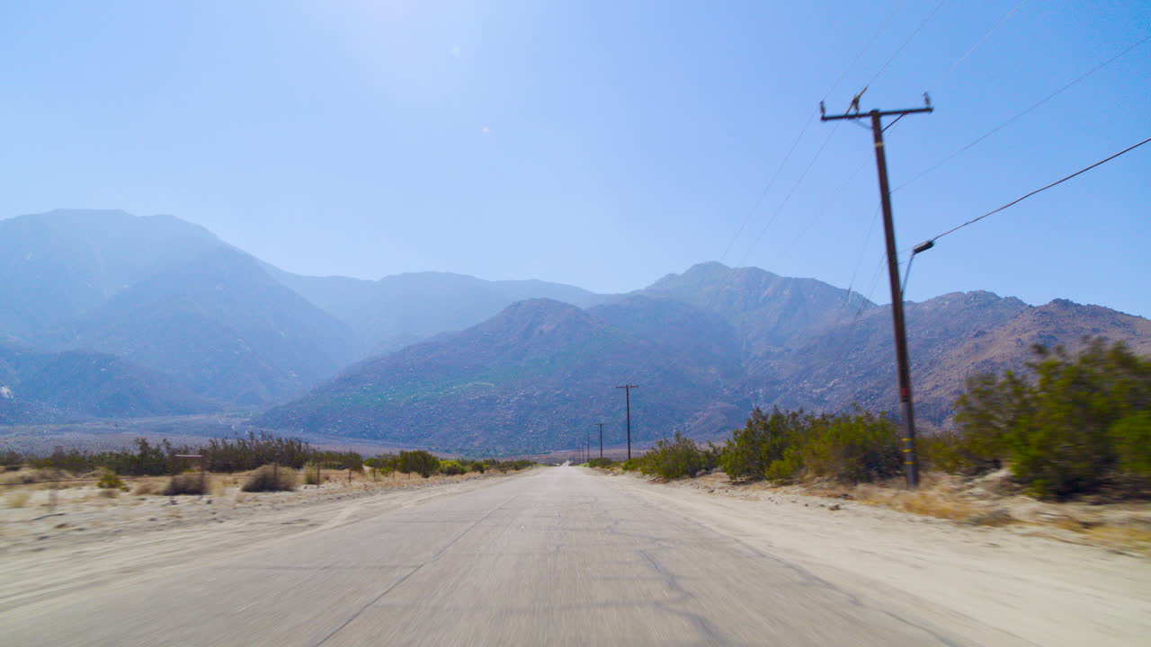 Palm Springs POV pan up from the road driving down the rugged San Jacinto Mountains in the distance in California under a clear blue sky on a bright, sunny day